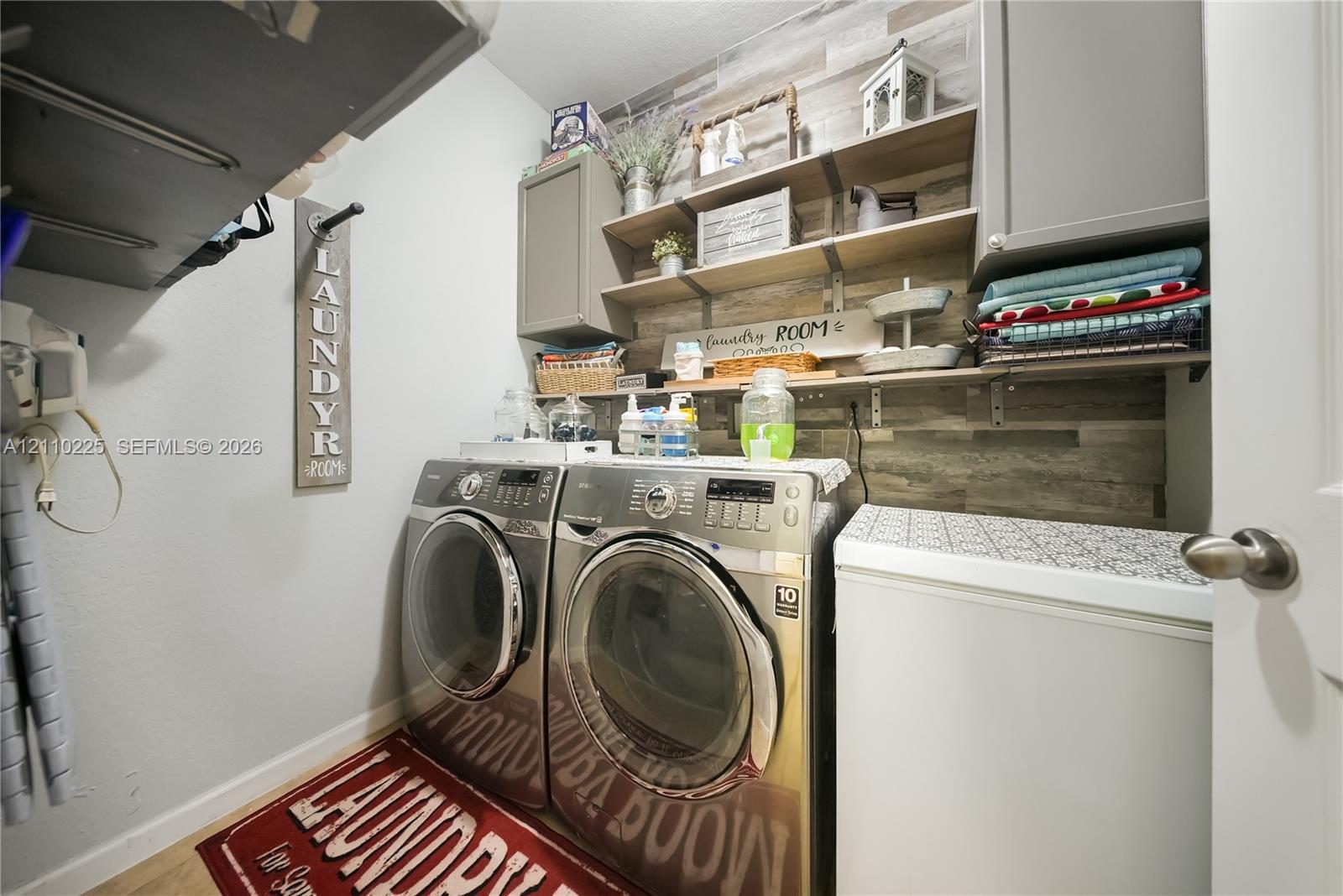 Laundry area featuring neutral wall-mounted cabinetry, open wood-finish shelving, and wood-patterned wall accents