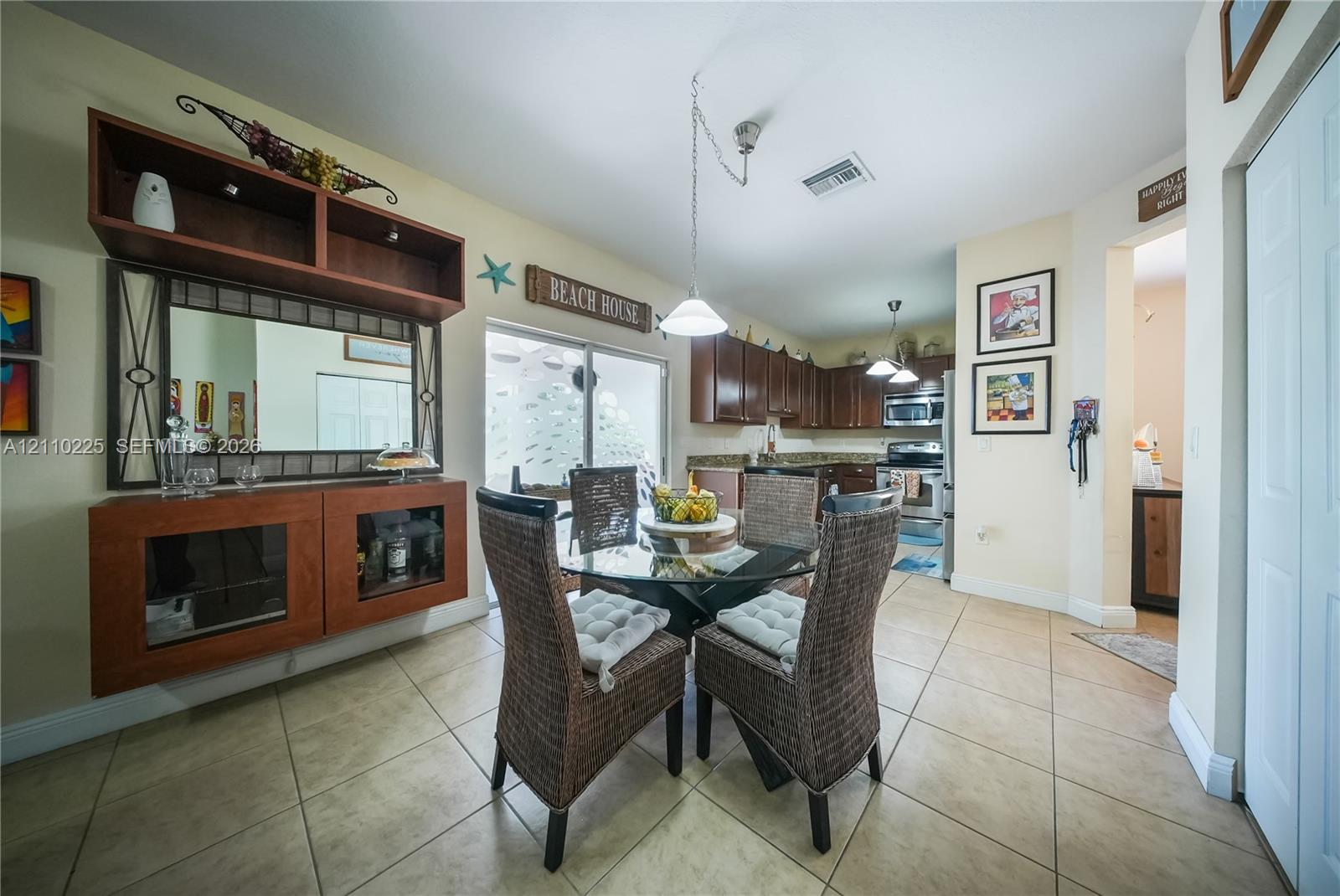 Kitchen area featuring wood cabinetry, stone countertops, stainless steel appliances, ceramic tile flooring, and built-in wall cabinetry with a mirror inlay