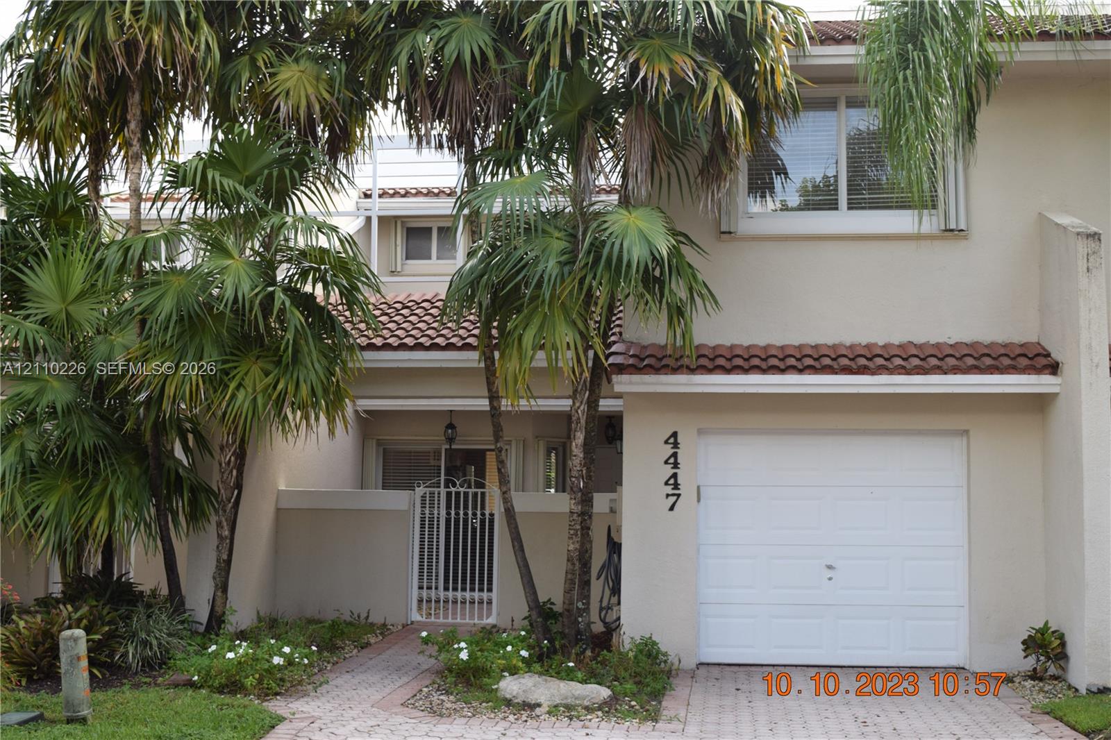Two-story exterior featuring a tile roof, single-car garage, brick paver driveway, and a gated courtyard entry