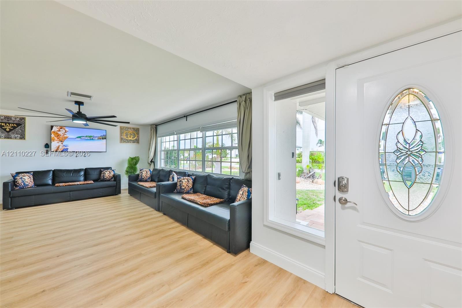 Entrance featuring a white door with an oval decorative glass insert, wood-finish flooring, multi-pane windows, and a black ceiling fan with integrated lighting