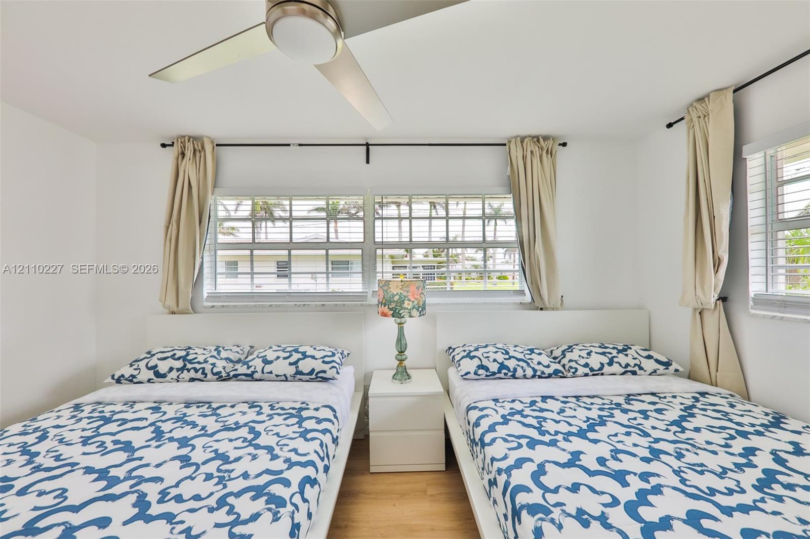 Room featuring wood-finish flooring, a contemporary ceiling fan with integrated lighting, and multiple horizontal sliding windows with metal rod hardware