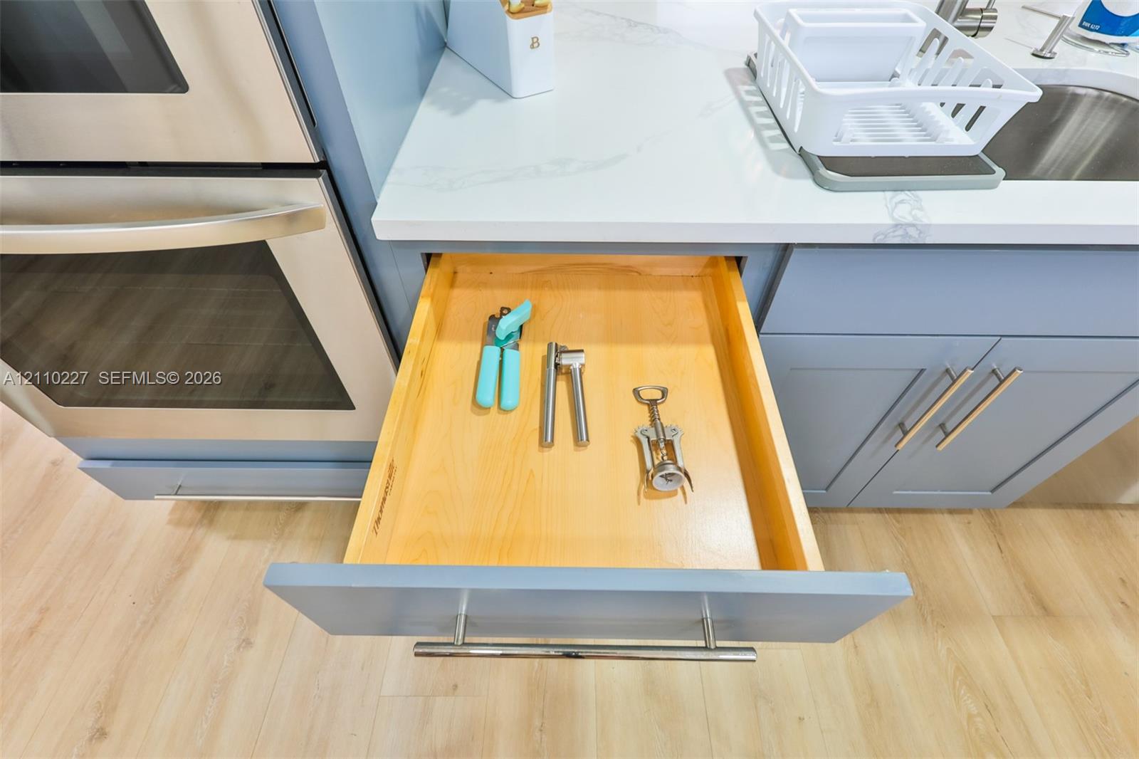Soft-close solid wood drawer with dovetail joinery, light-toned finish, stainless steel bar pull, quartz countertop, and integrated stainless steel wall oven