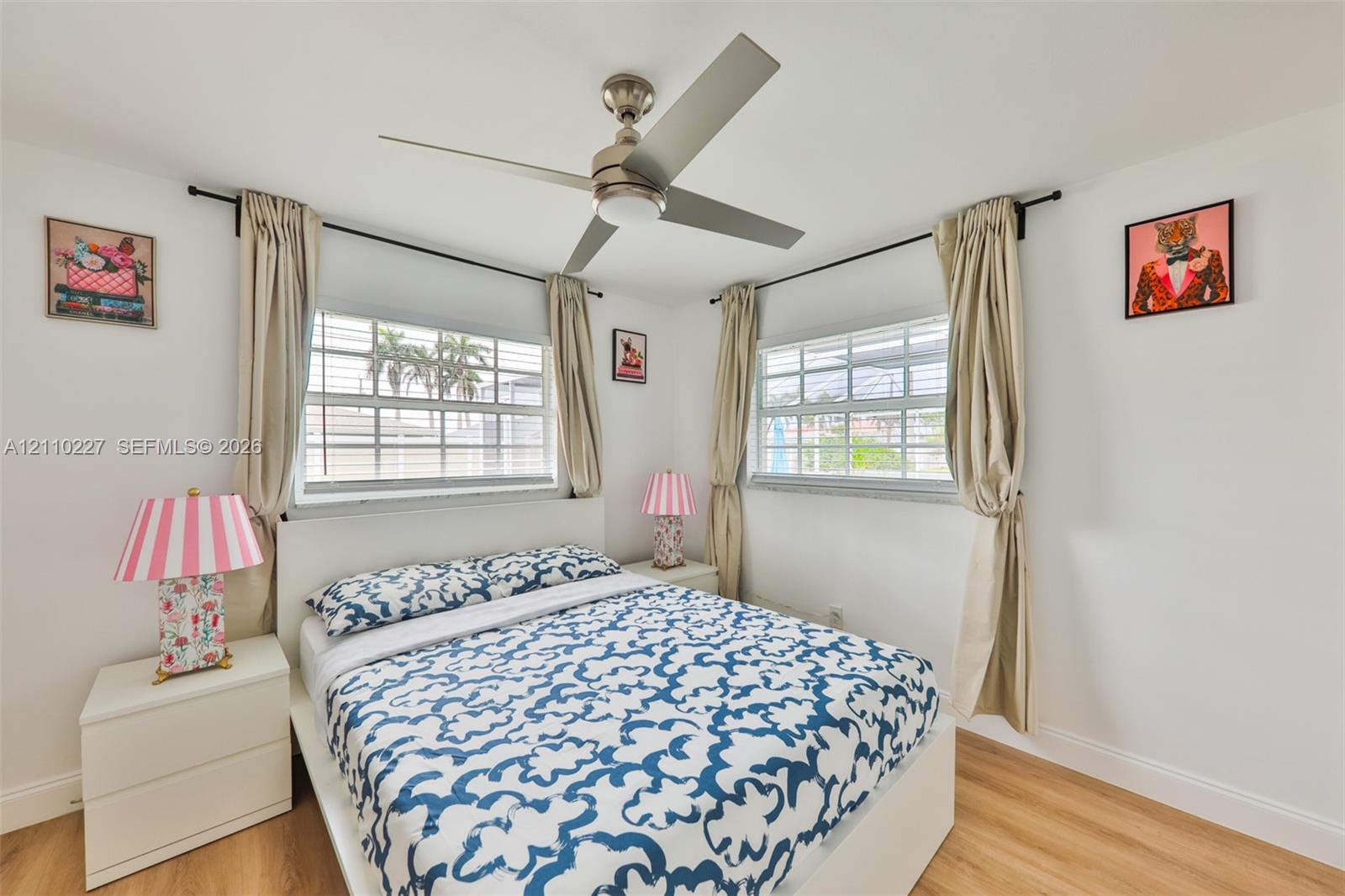 Neutral-toned interior featuring wood-finish flooring, dual windows with grid detailing, and a brushed-nickel ceiling fan with integrated lighting