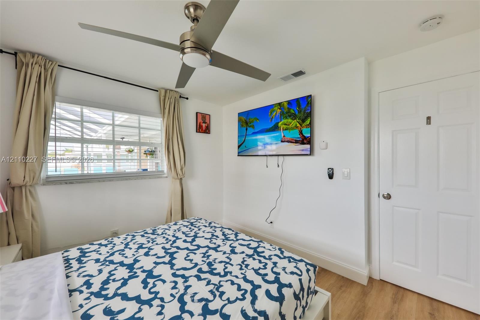 Neutral interior featuring wood-finish flooring, a contemporary brushed-metal ceiling fan, multi-pane window, and a six-panel door