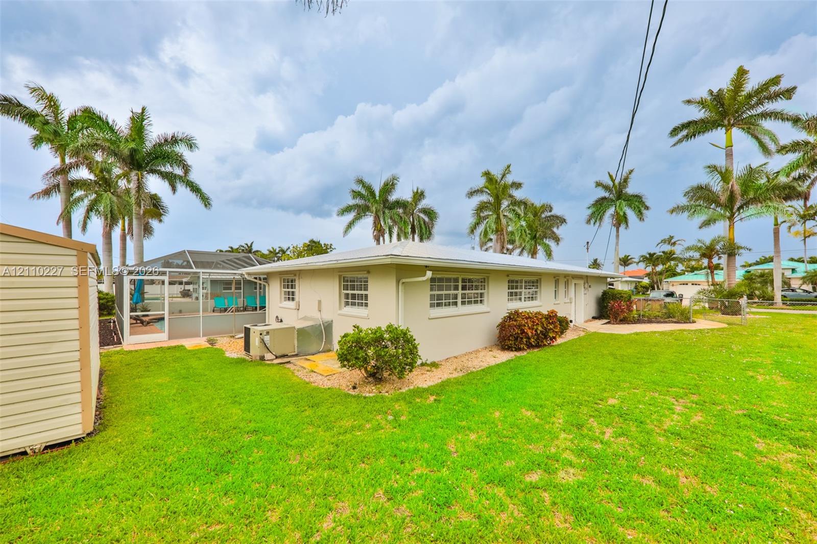 Exterior featuring a metal roof, screened-in enclosure, manicured lawn, established palm trees, and siding