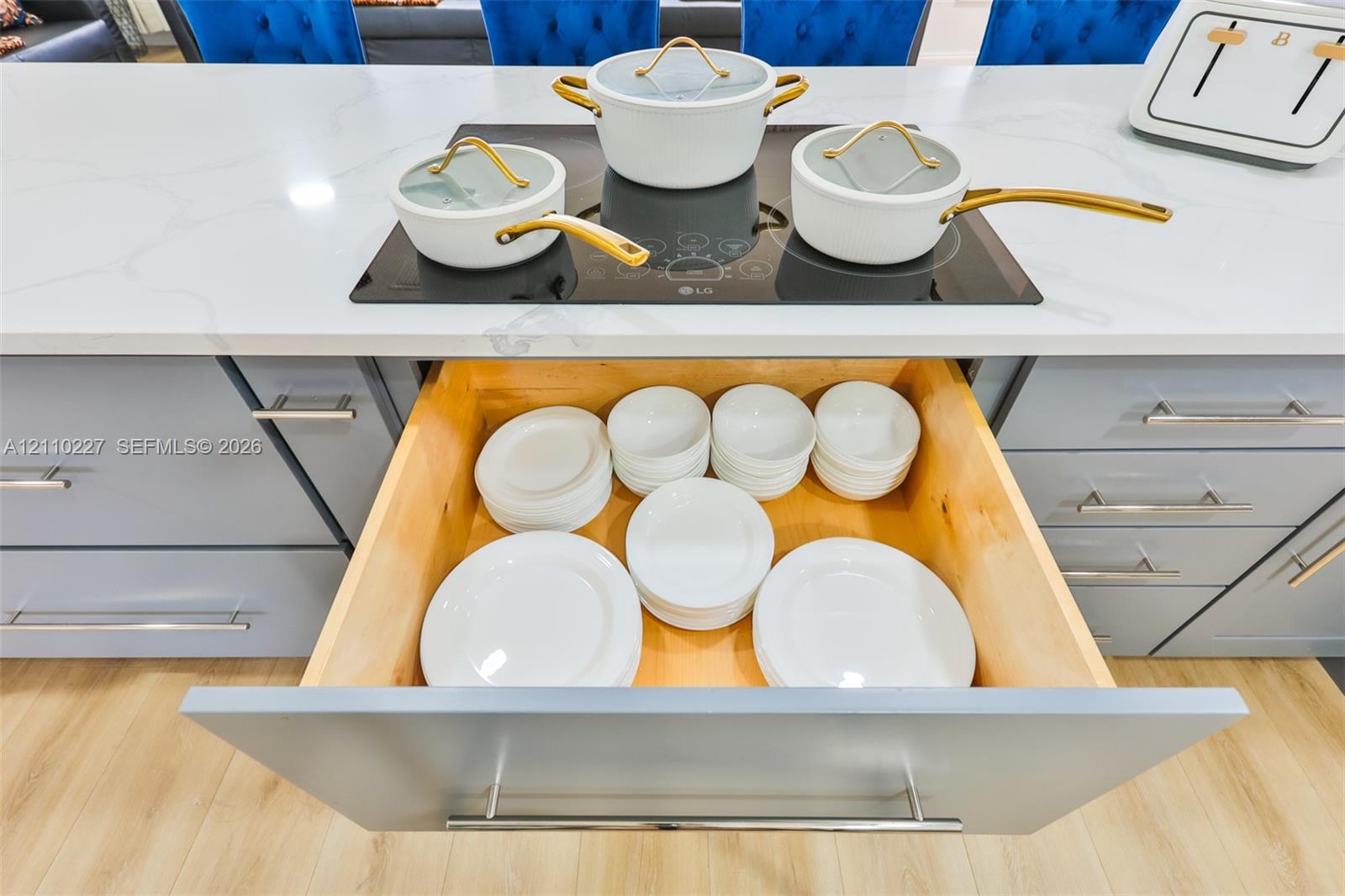 Kitchen island featuring a stone countertop with a flush-mounted induction cooktop, light-toned wood-finish flooring, and cabinetry with integrated pull-out drawer storage