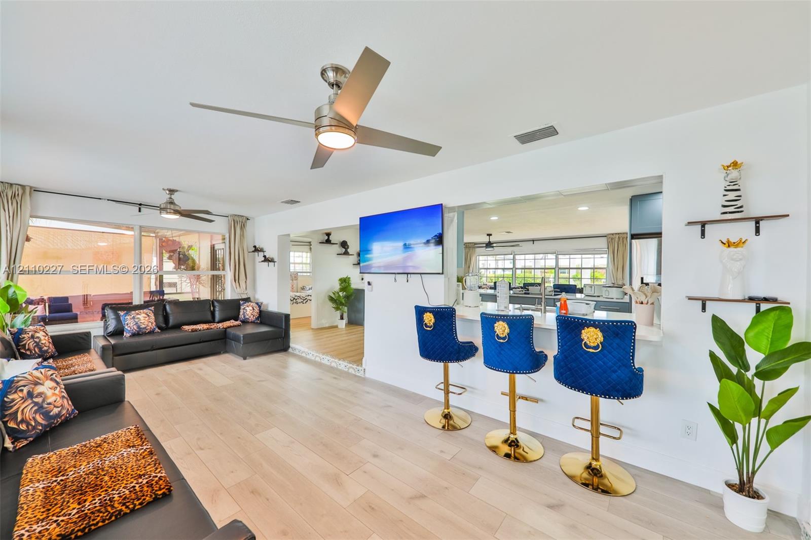 Open-concept interior featuring wood-finish flooring, brushed metal ceiling fans, and a breakfast bar with stone-surface counters
