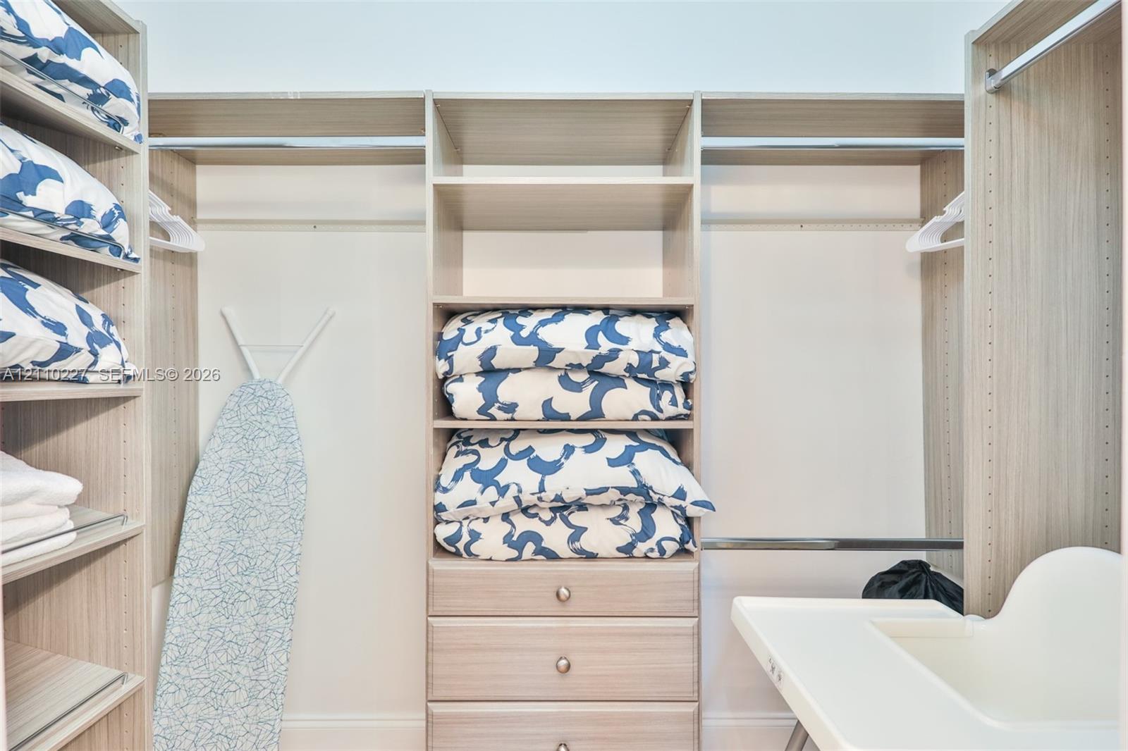 Custom walk-in closet featuring light-toned wood-finish cabinetry, adjustable open shelving, integrated hanging rods, and a three-drawer built-in chest
