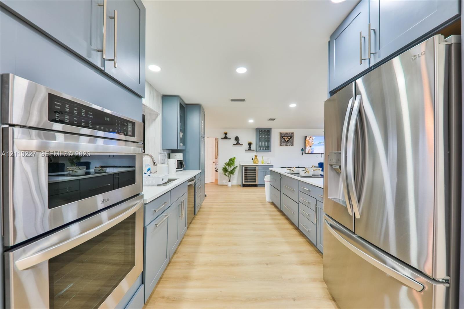 Kitchen featuring wood-finish flooring, stainless steel appliances, dual wall ovens, blue shaker-style cabinetry, and recessed lighting