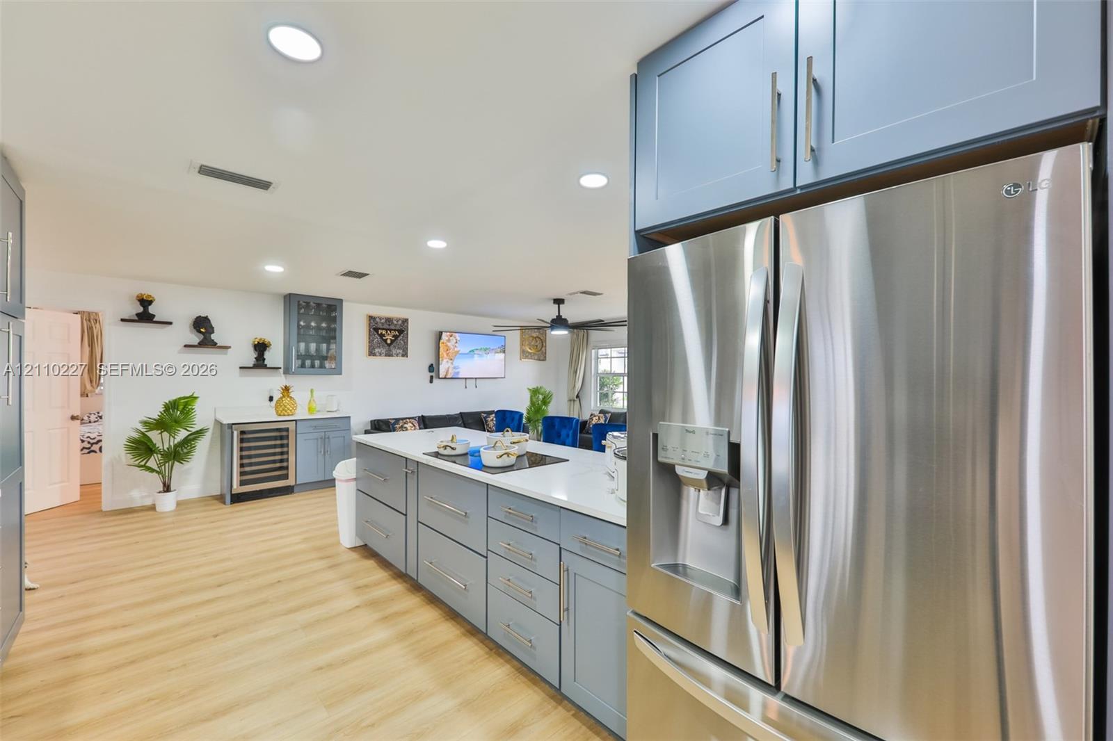 Kitchen featuring stainless steel refrigerator, large central island with light-toned countertop, built-in beverage cooler, shaker-style cabinetry, and wood-finish flooring