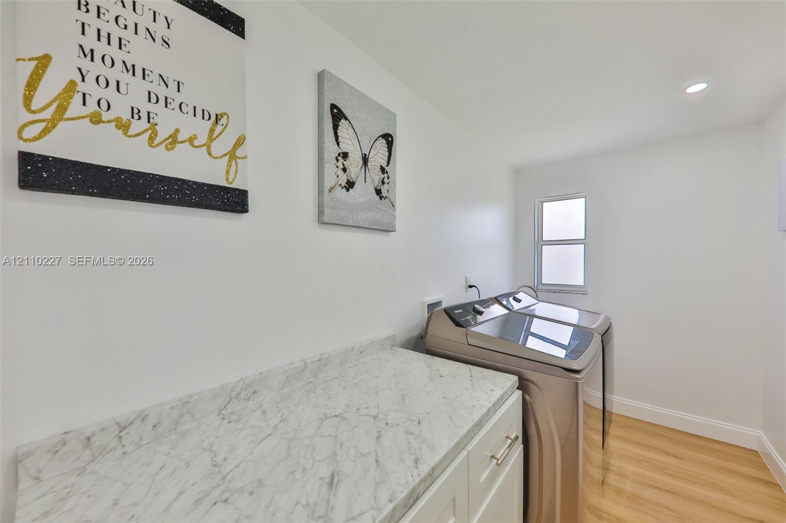 Laundry area featuring white cabinetry, light-toned stone-finish countertop with matching backsplash, wood-finish flooring, and recessed ceiling lighting
