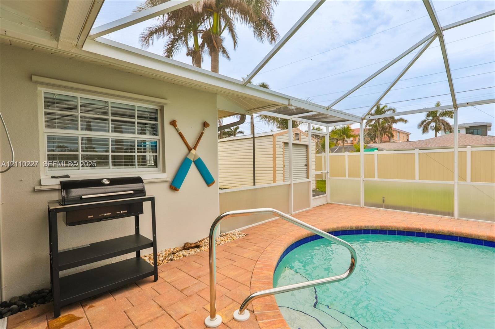 Screened-in enclosure featuring a private pool with a paved deck, perimeter privacy fencing, and exterior storage structure