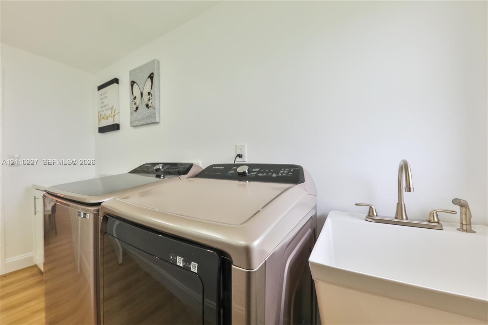Laundry area featuring a drop-in utility sink with a high-arch faucet, side-by-side washer and dryer, white cabinetry, and wood-finish flooring