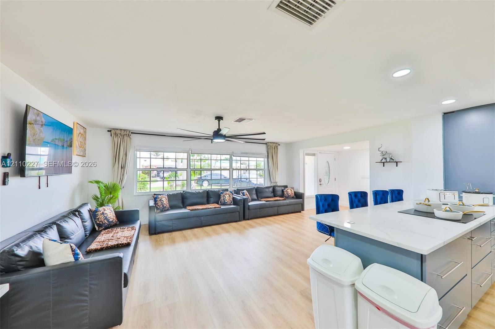 Open-concept interior featuring light wood-finish flooring, recessed lighting, a ceiling fan, and a center island with a stone-surface countertop and cabinetry