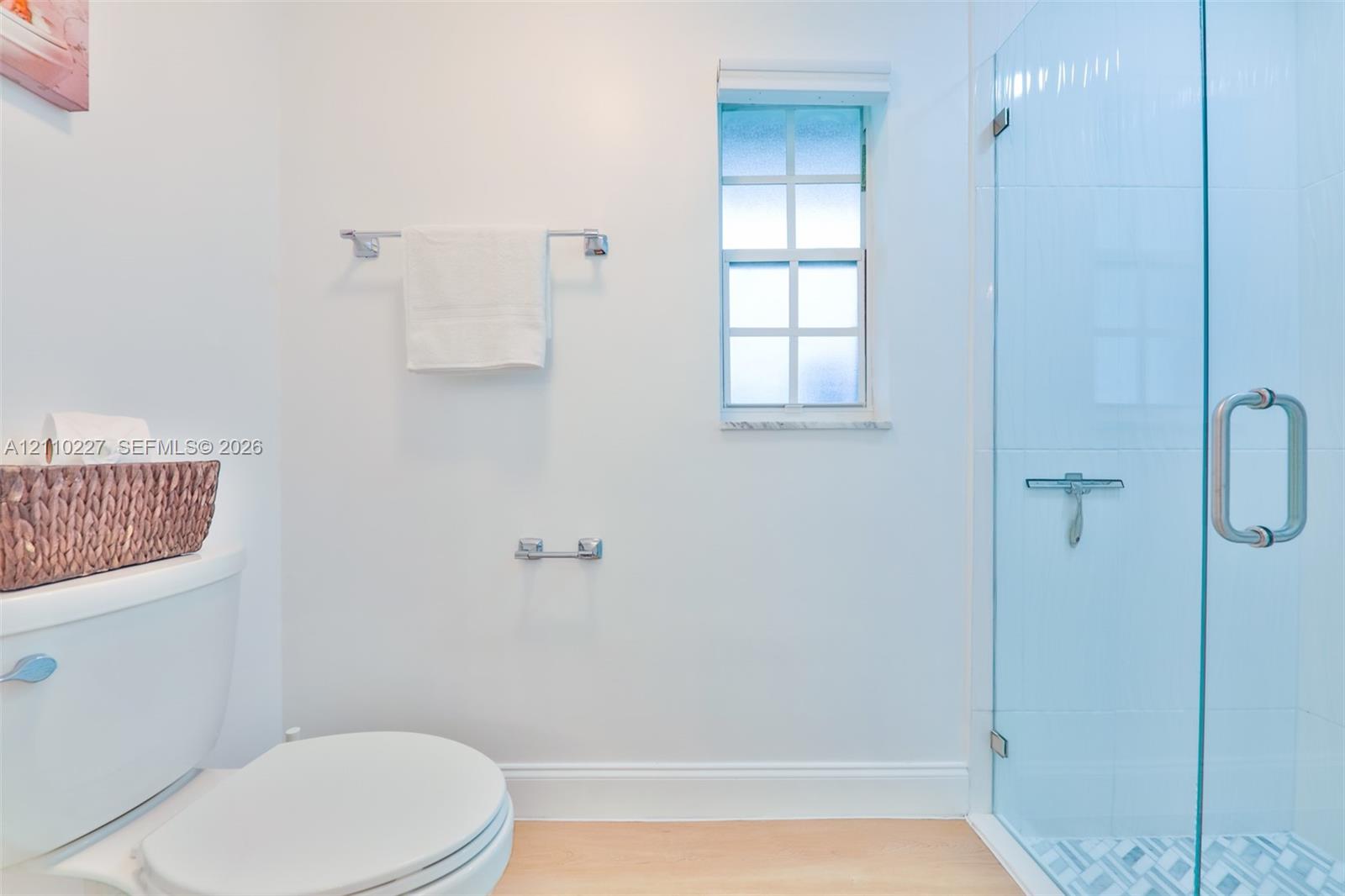 Shower enclosure with a frameless glass door, light-toned wood-finish flooring, and a window with muntins