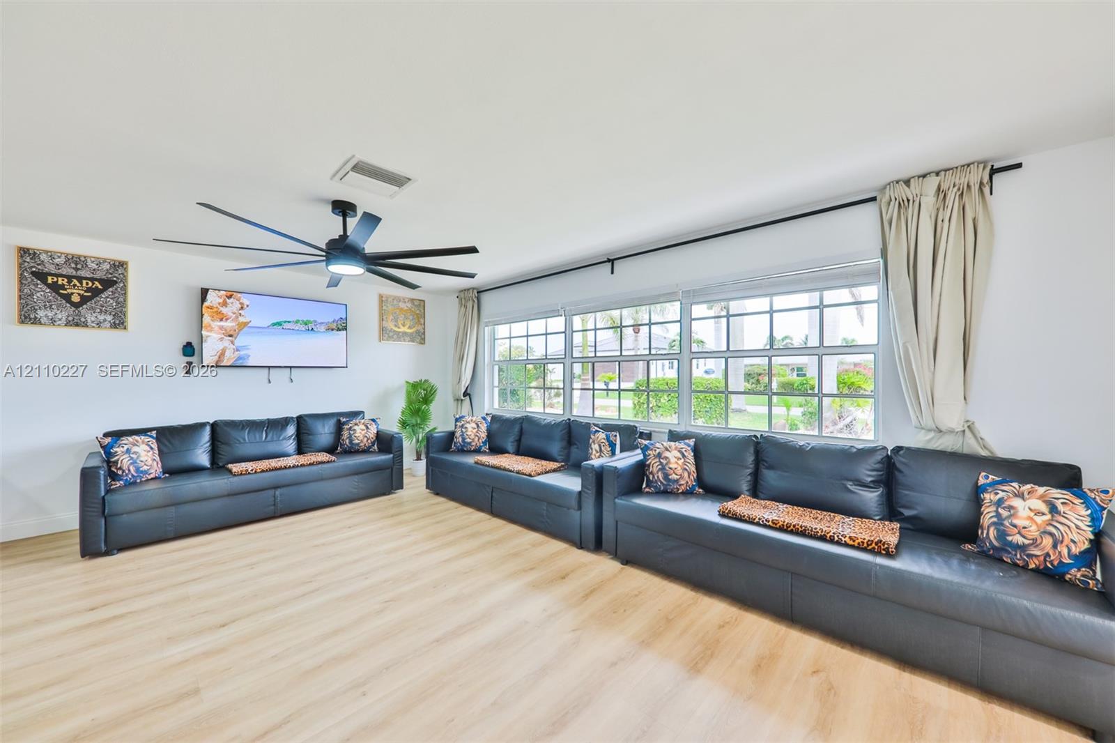 Living area featuring wood-finish flooring, a contemporary multi-blade ceiling fan, and expansive windows with grid-pattern muntins