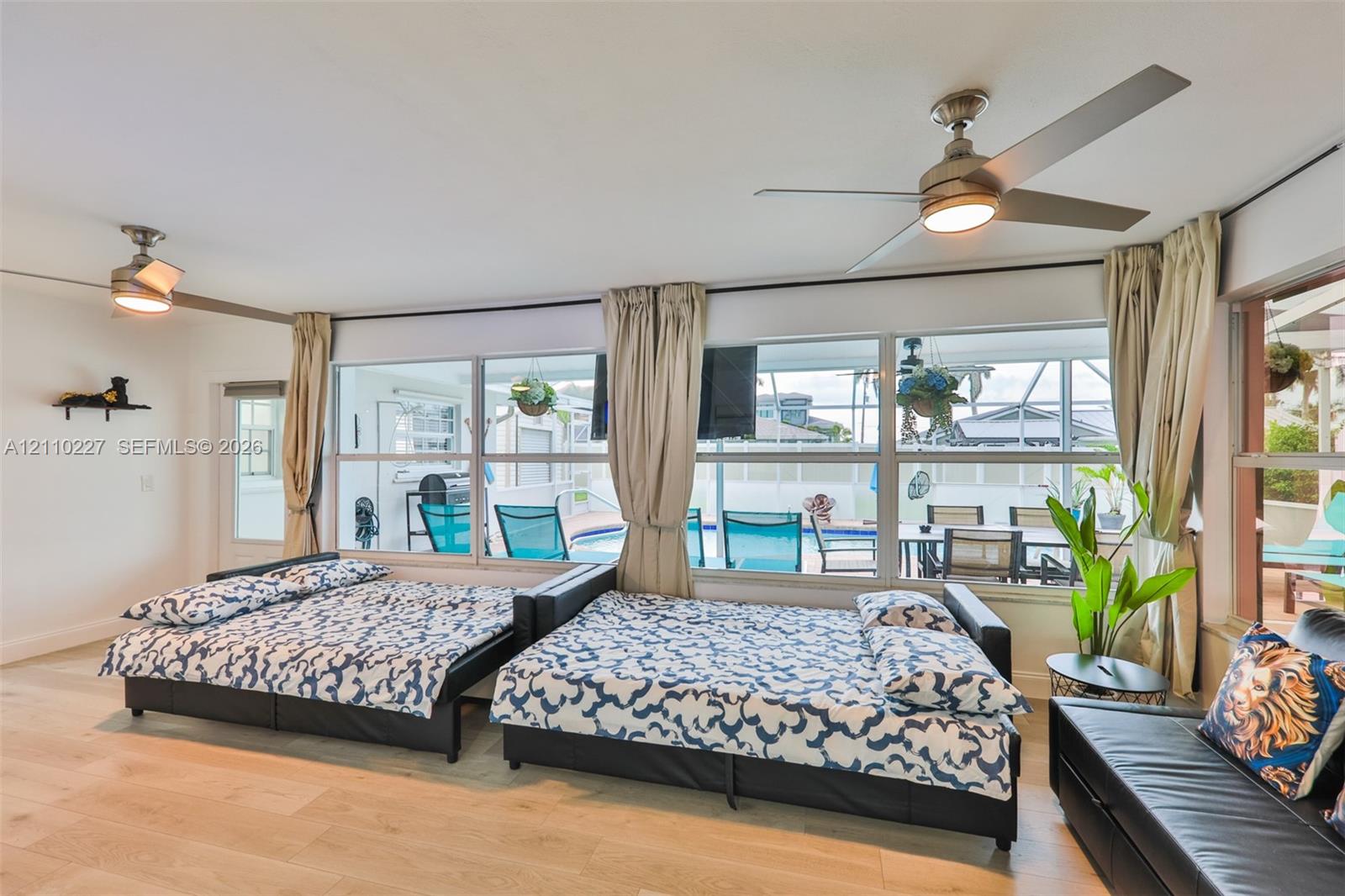 Spacious room featuring wood-finish flooring, two ceiling fans with integrated lighting, and a wall of floor-to-ceiling windows