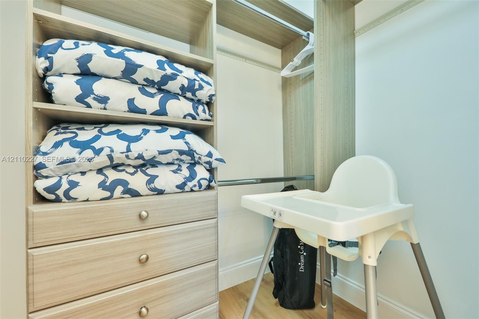Built-in closet organizer featuring light wood-finish cabinetry, integrated shelving, three lower drawers with round hardware, and a metal hanging rod