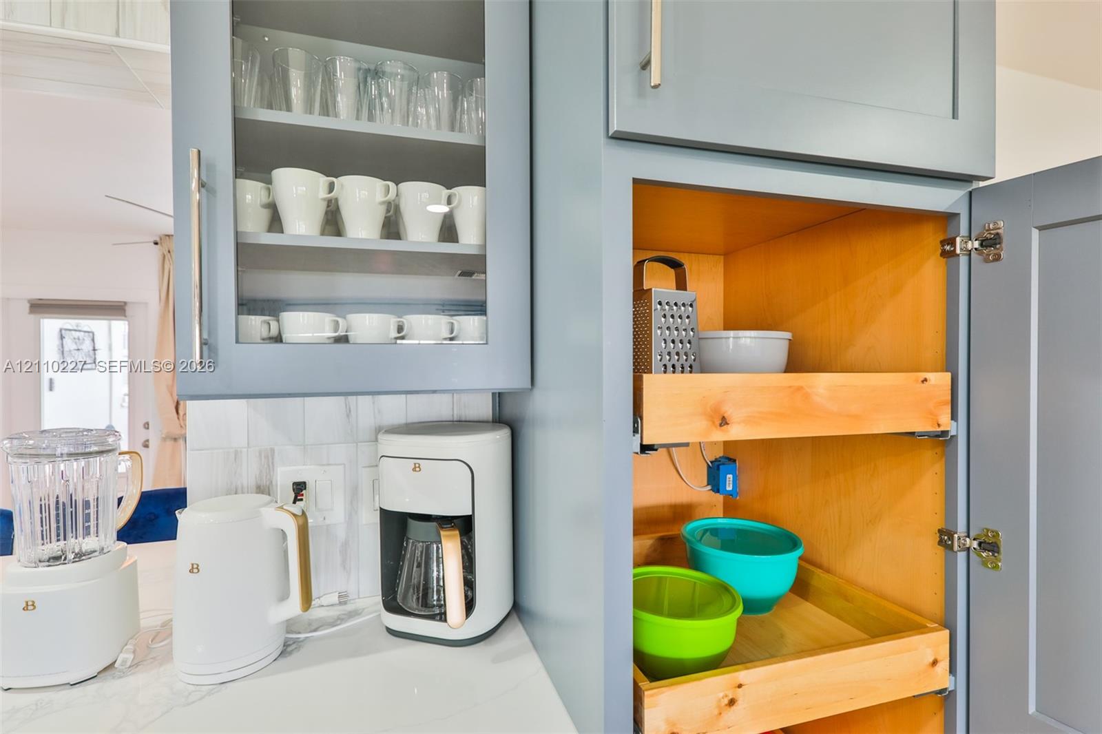 Custom cabinetry featuring shaker-style doors, glass-front upper storage, and built-in sliding wooden drawers, complemented by a stone-surface countertop and a tile backsplash