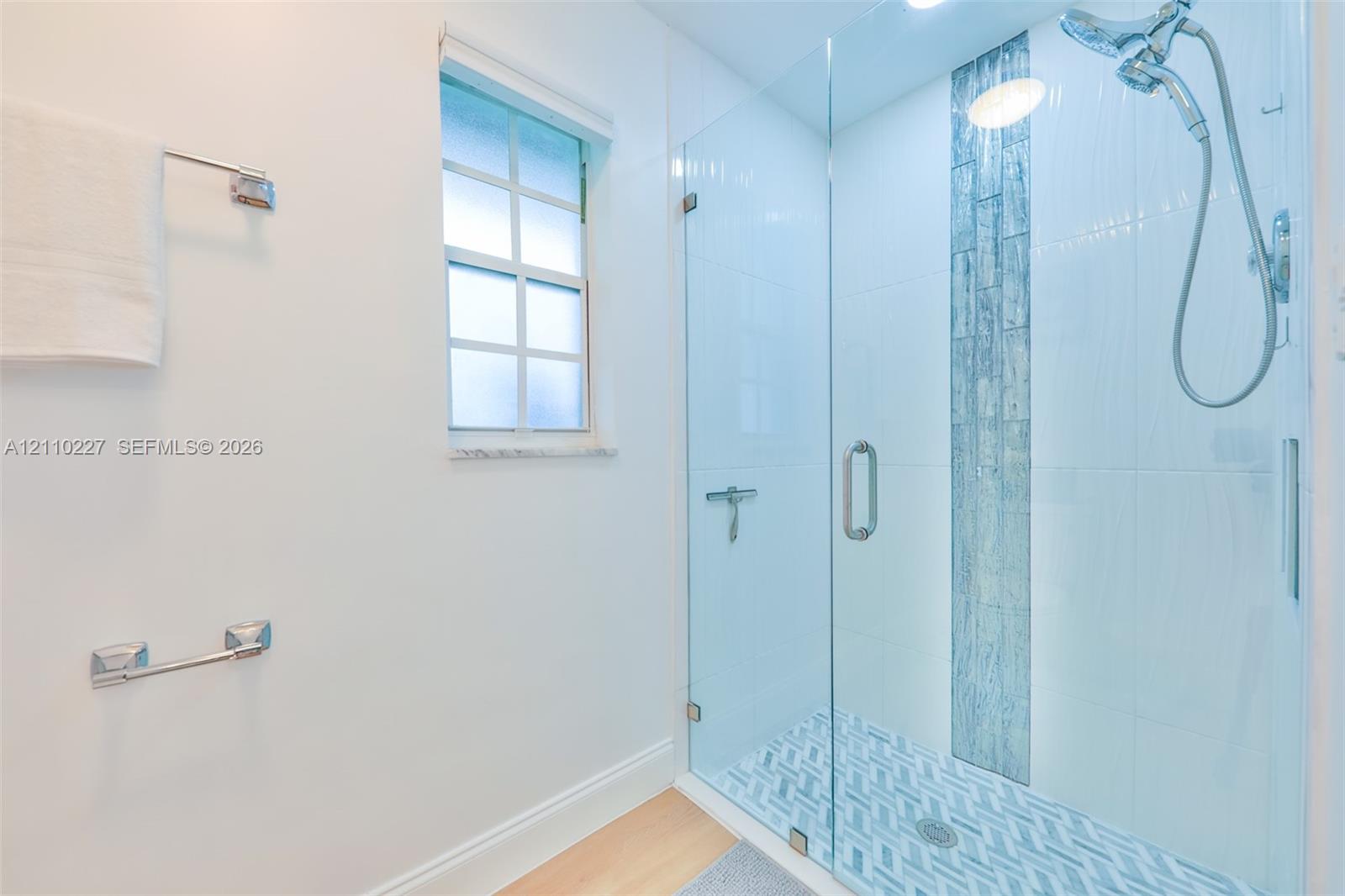 Walk-in shower featuring a glass enclosure, vertical decorative tile inlay, patterned tile flooring, and a multi-function showerhead