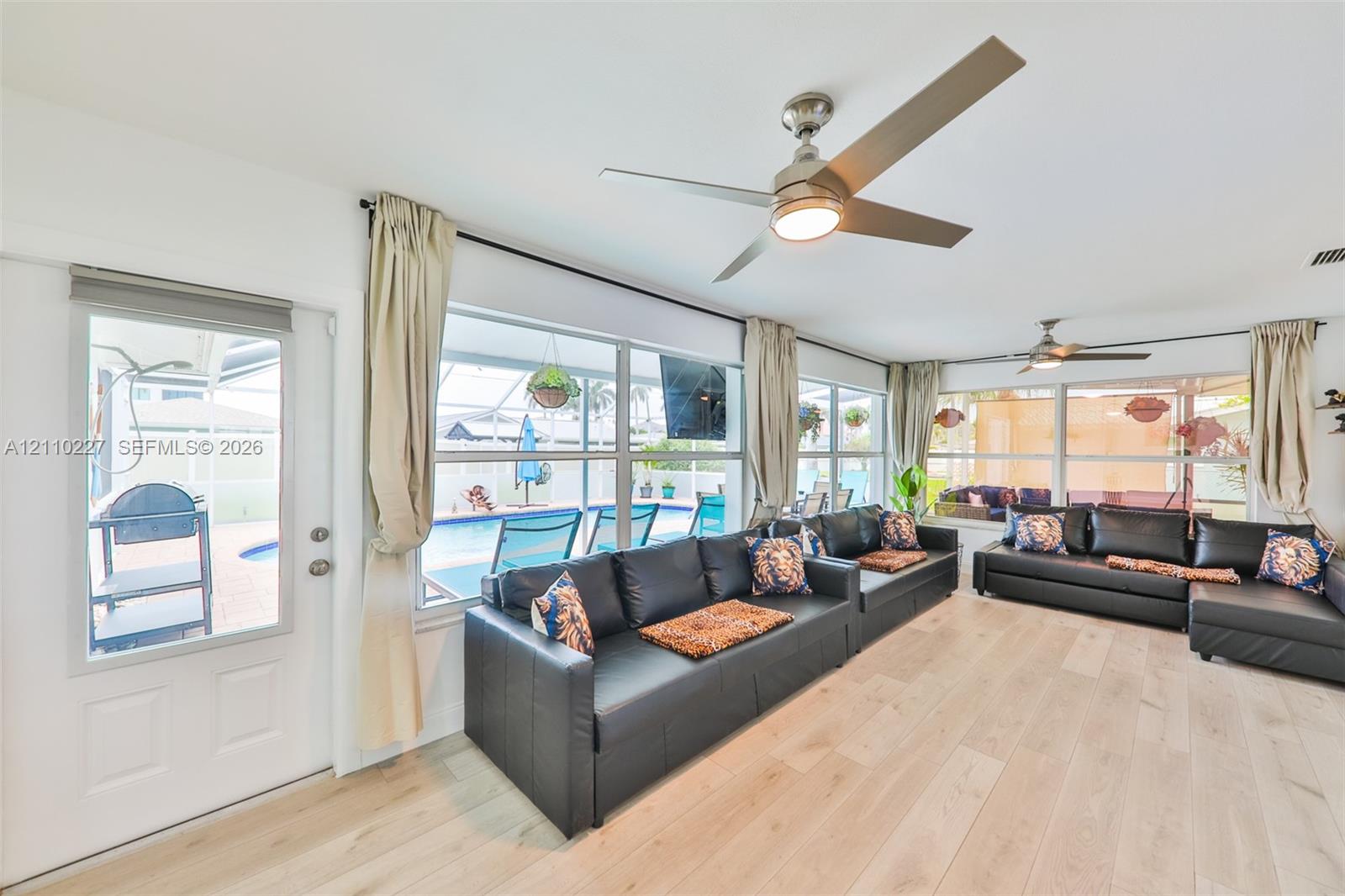 Light-filled sunroom featuring wood-finish flooring, dual ceiling fans, expansive windows, and a glass-paneled entry door