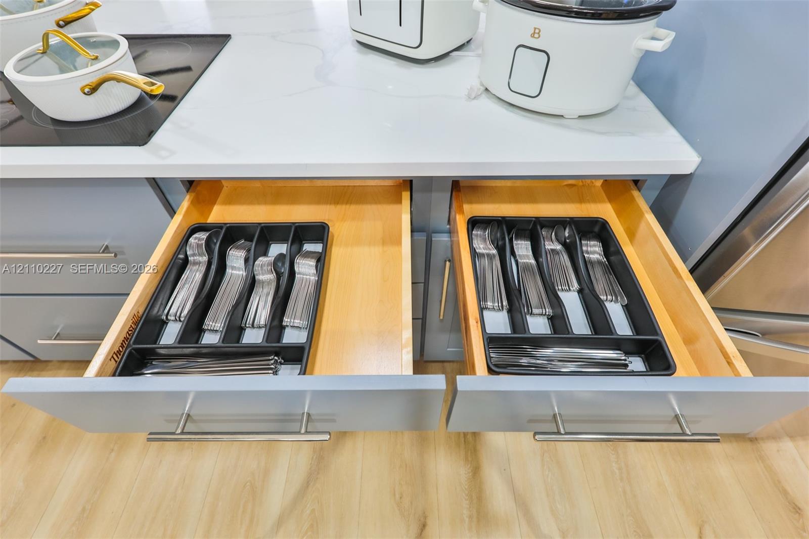 Shaker-style cabinetry featuring integrated drawer organizers, wood-finished interior drawer boxes, stone-composite countertops, and satin-finish metal hardware
