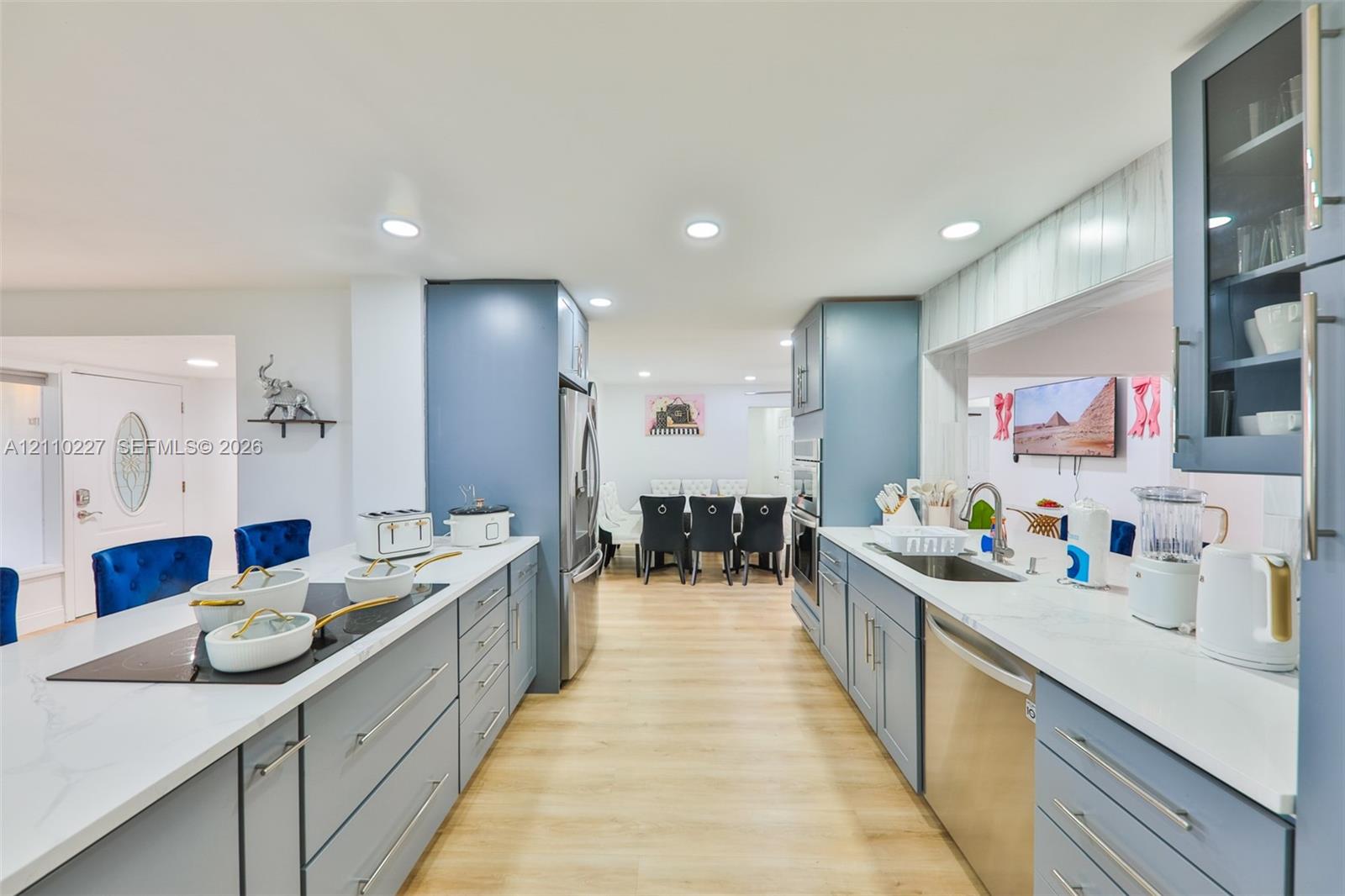 Kitchen featuring light blue cabinetry, stone-finish countertops, stainless steel appliances, a built-in cooktop, and wood-finish flooring