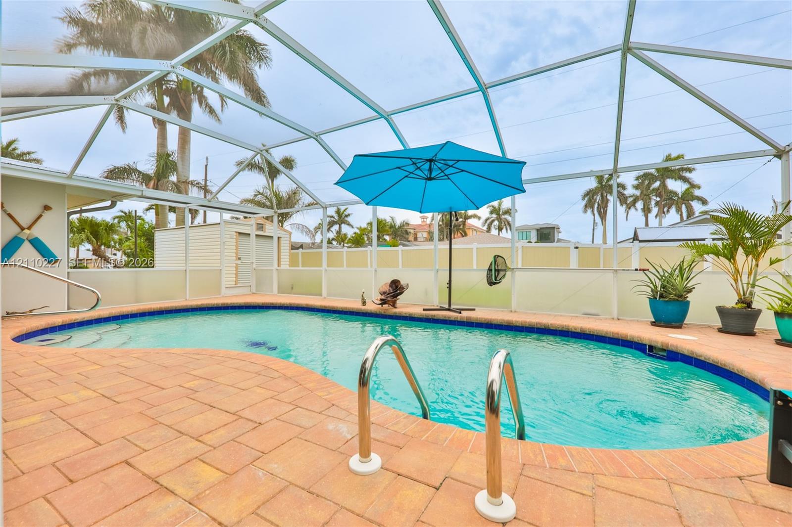Screened-in pool area featuring paver decking, curved pool architecture with built-in stairs, metal handrails, and a detached storage structure