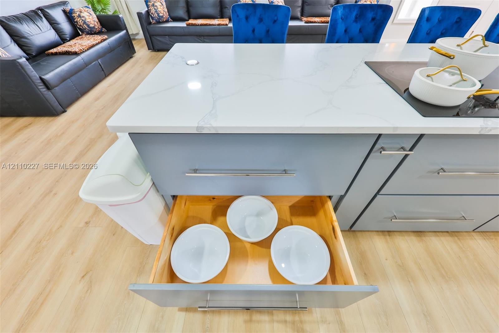 Center island featuring a stone-look countertop, integrated electric cooktop, light blue cabinetry with brushed metal hardware, and soft-close pull-out drawers with natural wood interiors, finished with wood-tone flooring