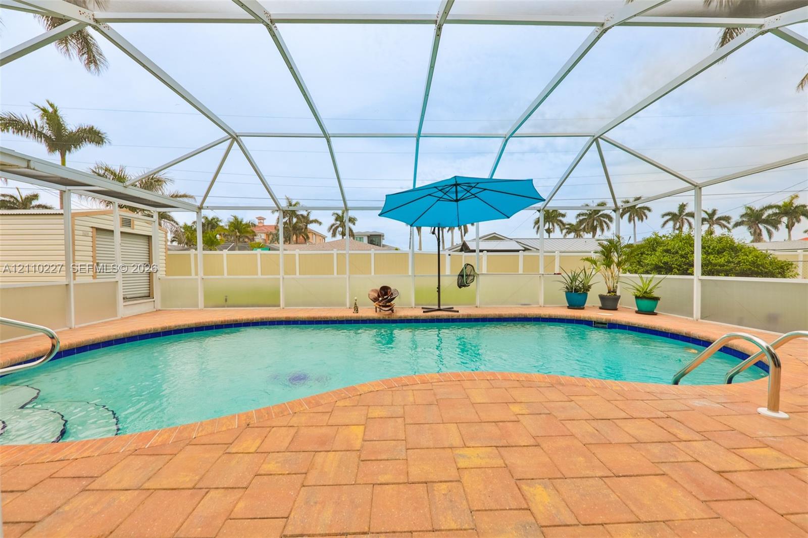 Screened-in outdoor living space featuring an inground pool with paver decking and metal handrails