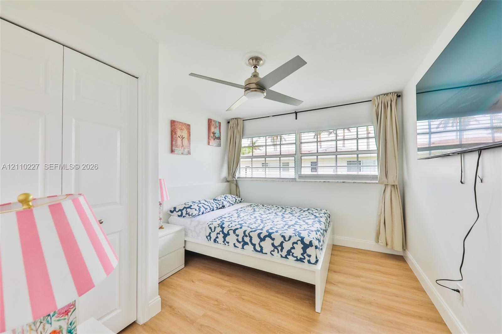 Light-filled room featuring wood-finish flooring, a multi-blade ceiling fan, multi-pane windows, and dual-panel closet doors