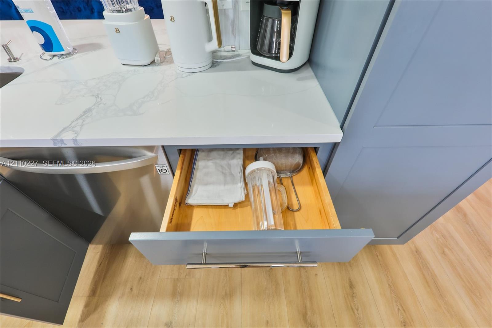 Custom shaker-style cabinetry with soft-close drawer functionality, polished stone-finish countertops, stainless steel appliances, and wood-finish flooring