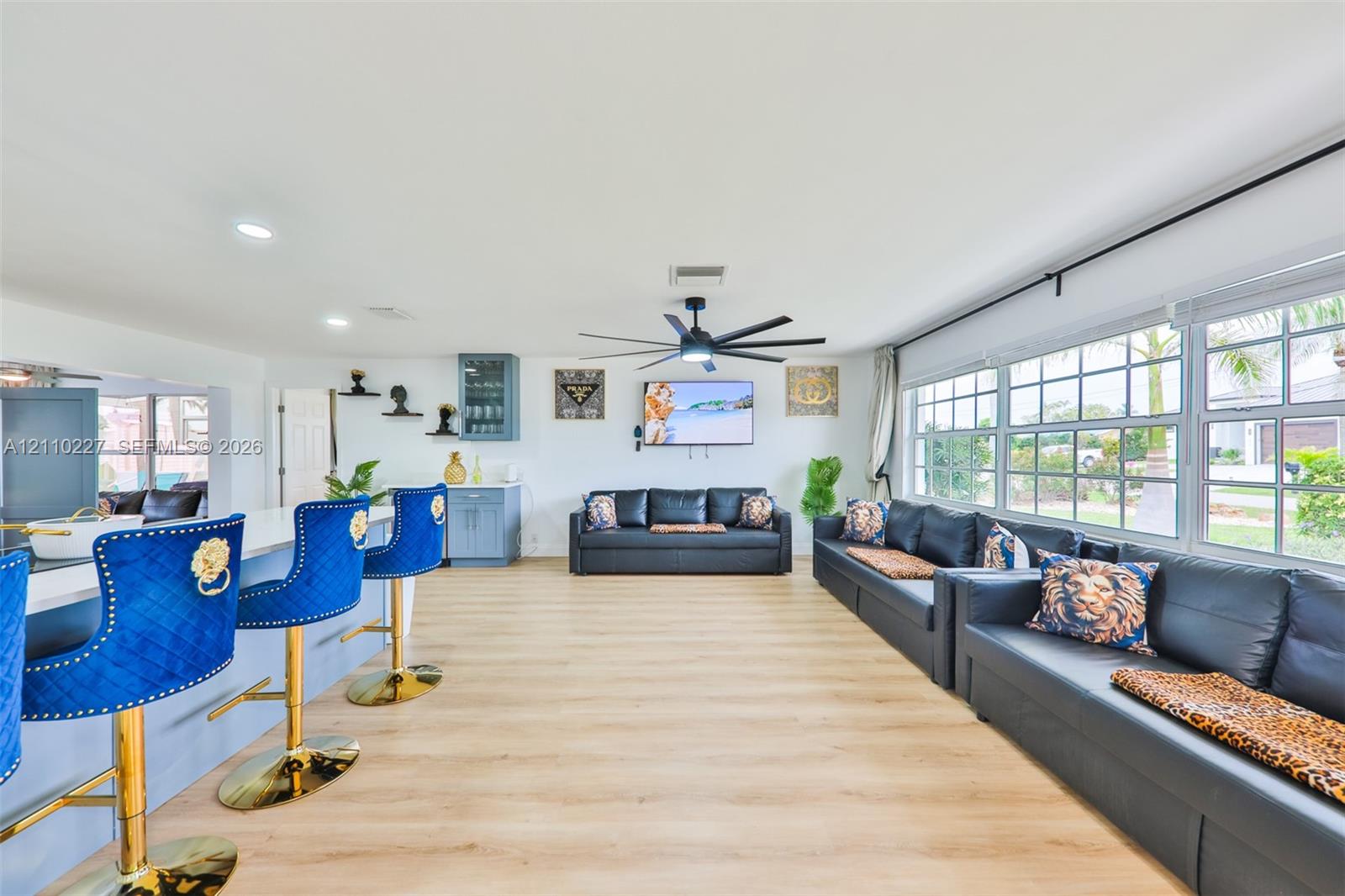 Open-concept interior featuring light-toned wood-finish flooring, recessed lighting, multi-blade ceiling fan, and large windows with grid muntins