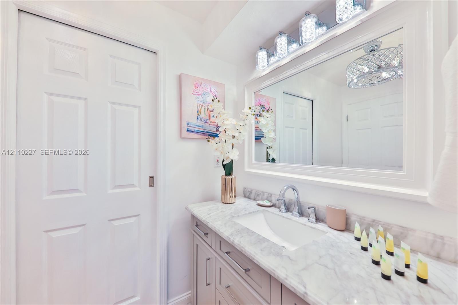Vanity featuring a stone-look countertop with an integrated rectangular basin, contemporary metallic faucet, recessed cabinetry, and a large, framed mirror with integrated multi-bulb lighting