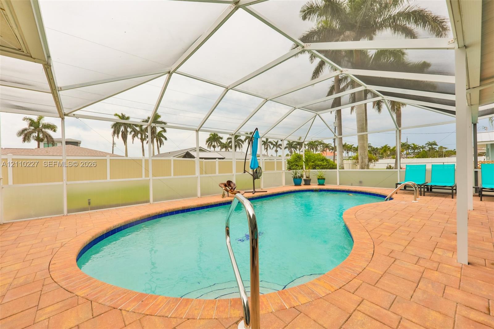 Screened-in patio featuring a kidney-shaped swimming pool, brick paver decking, and a metal pool ladder