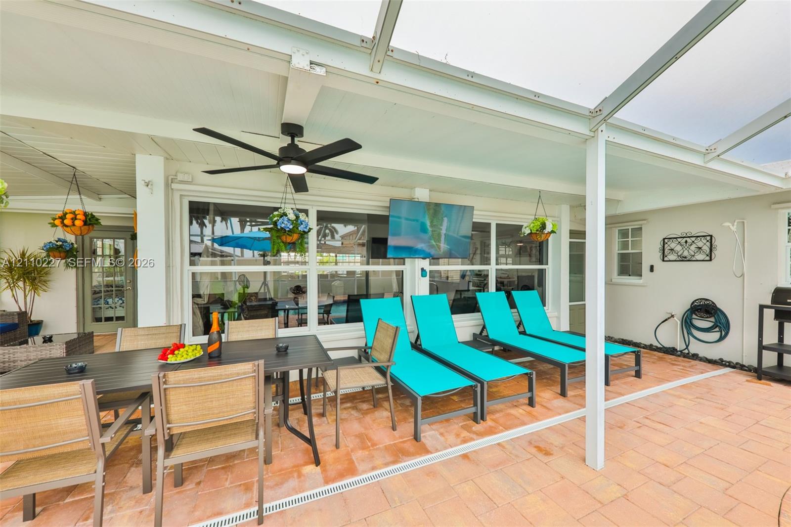 Covered patio featuring paver flooring, a screened enclosure, a ceiling-mounted fan, and a wall-mounted television