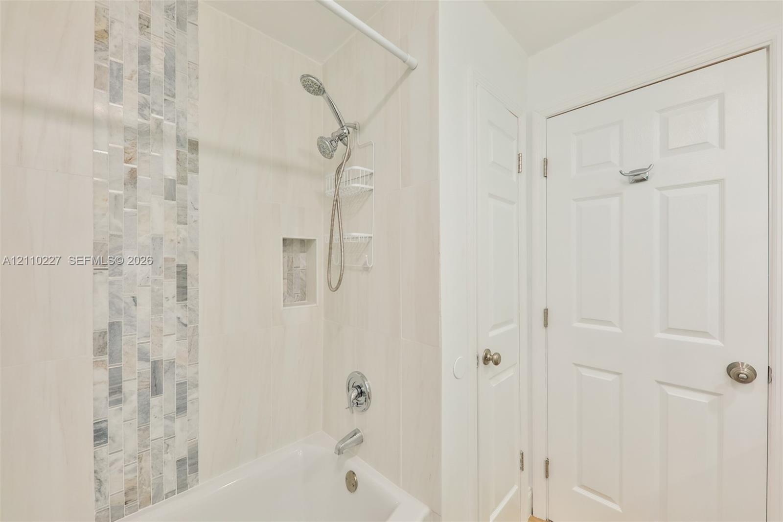 Bathtub and shower combination featuring large-format wall tile, a vertical decorative stone mosaic accent, an integrated wall niche, and polished chrome fixtures