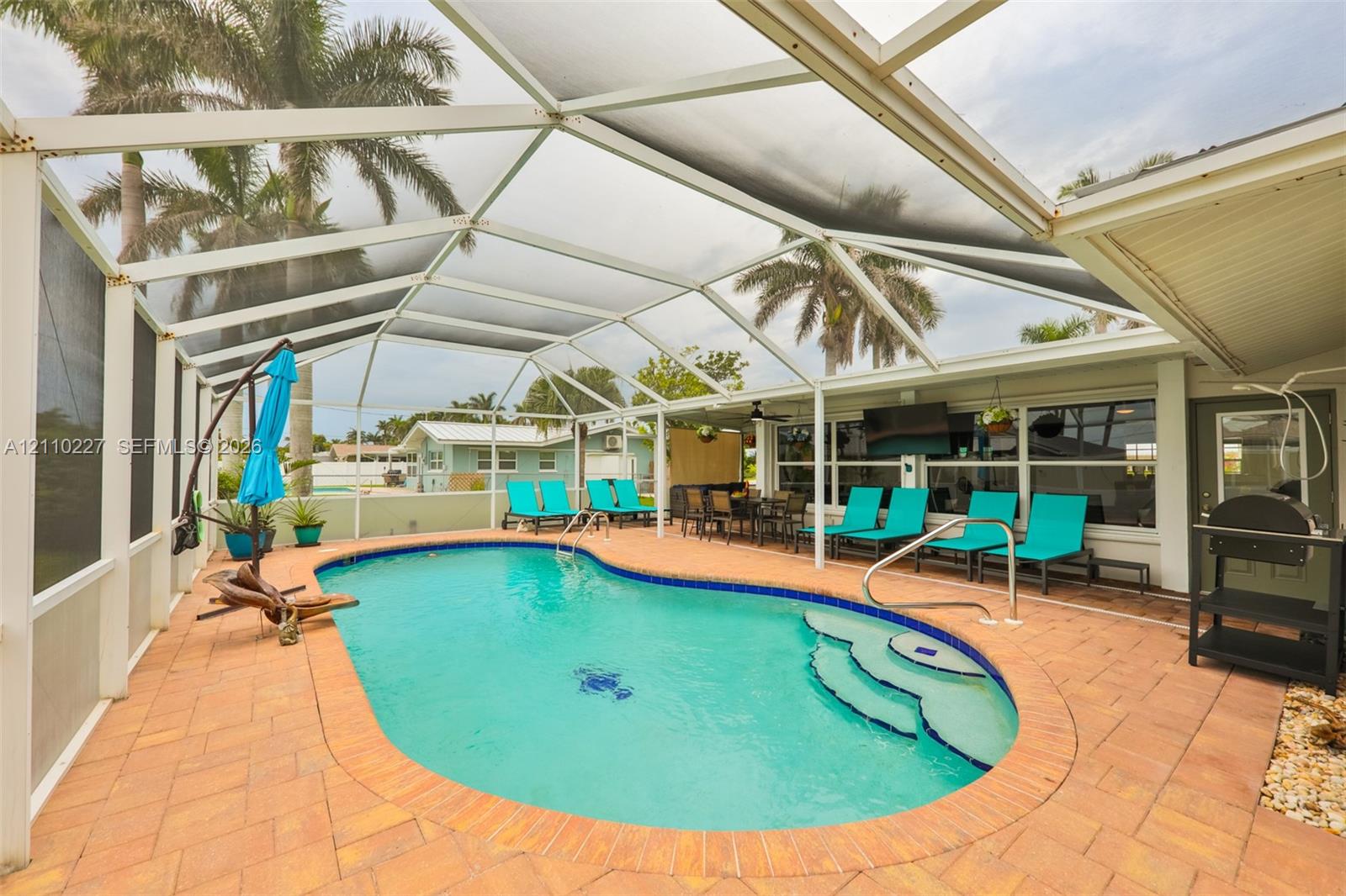 Screened-in patio featuring a kidney-shaped swimming pool, built-in steps, and expansive brick paver decking