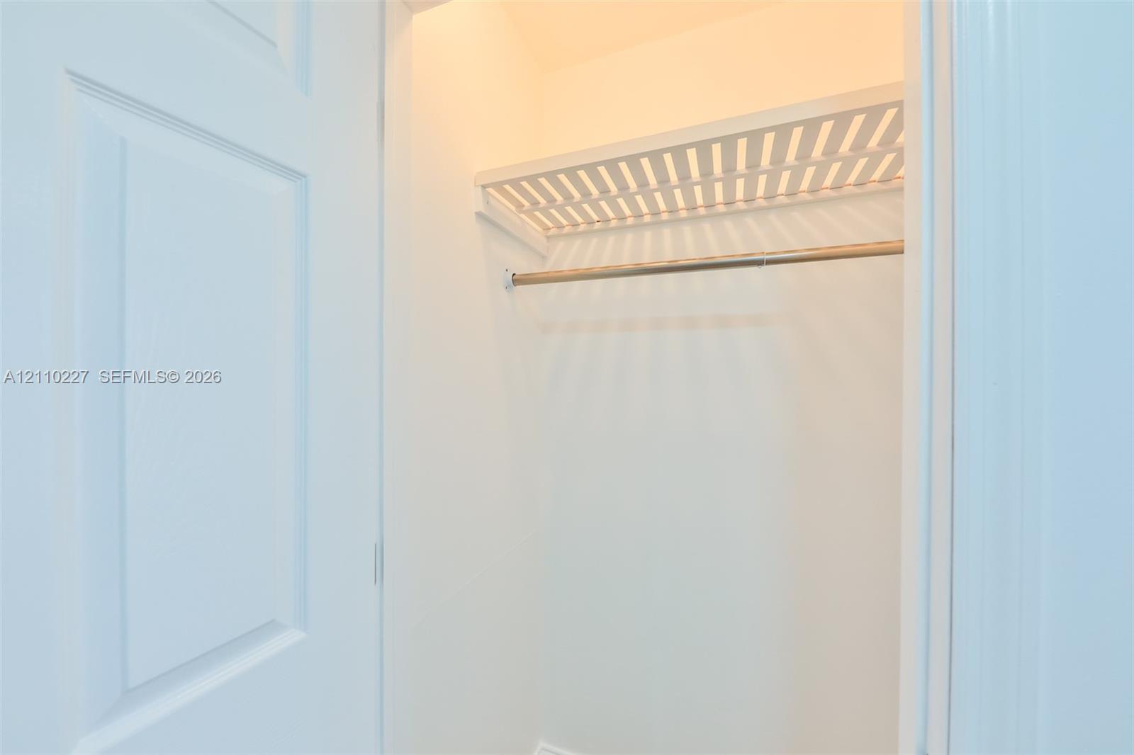 Interior closet featuring a white paneled door, built-in slatted shelving, and a metal hanging rod