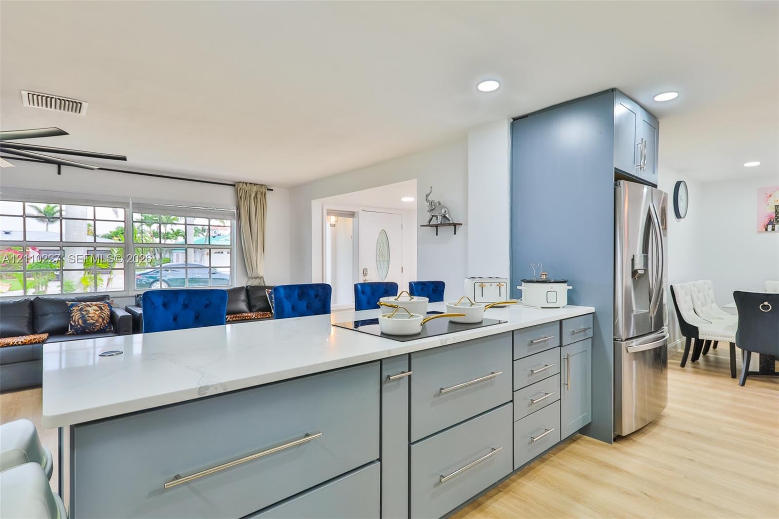 Kitchen featuring a quartz countertop, blue cabinetry with brushed metal pulls, stainless steel refrigerator, recessed lighting, and wood-finish flooring