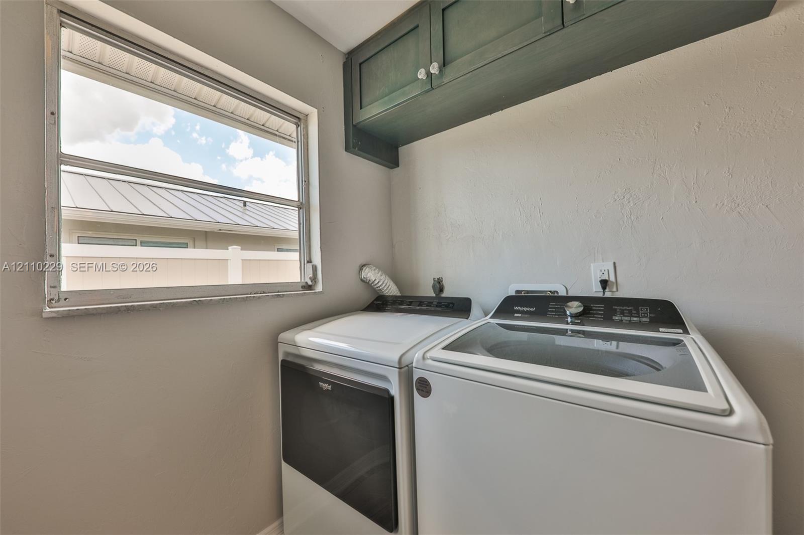 Laundry area featuring dark-finished upper cabinetry, a single-pane window, and white finish laundry appliances