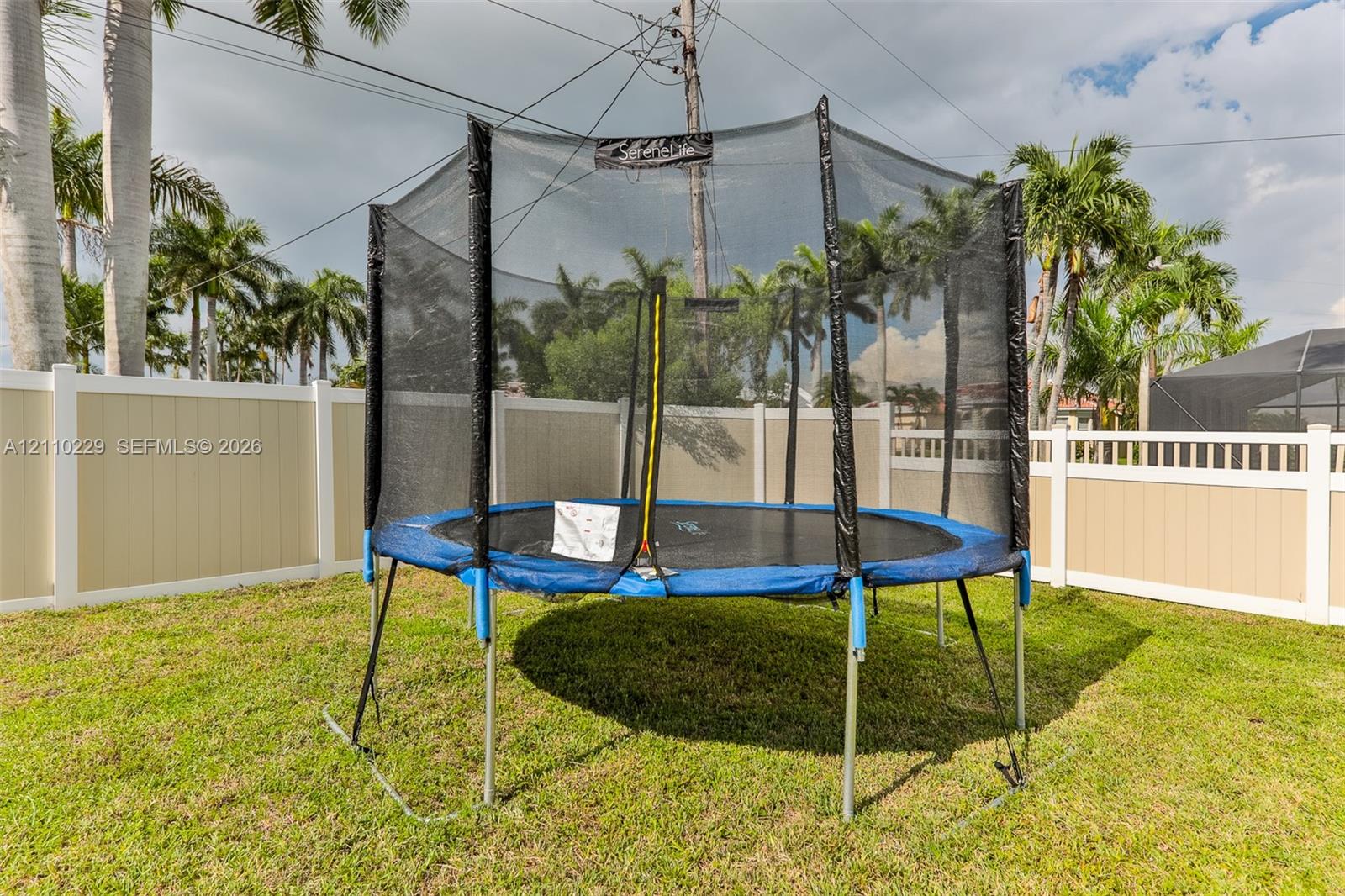 Rear yard featuring a grass lawn enclosed by white vinyl fencing and mature palm trees
