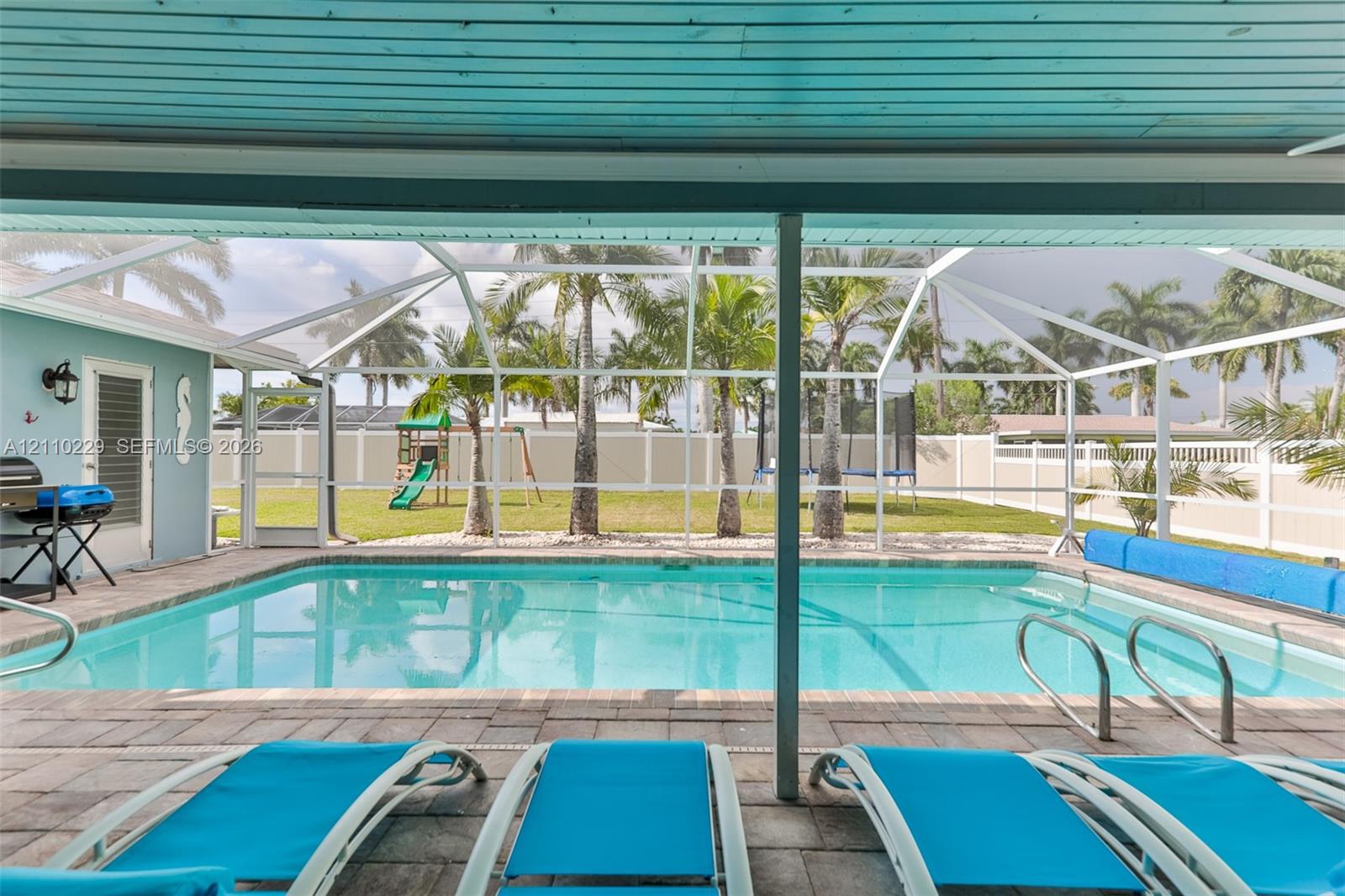 Screened-in outdoor area featuring a swimming pool, brick paver decking, and a privacy fence