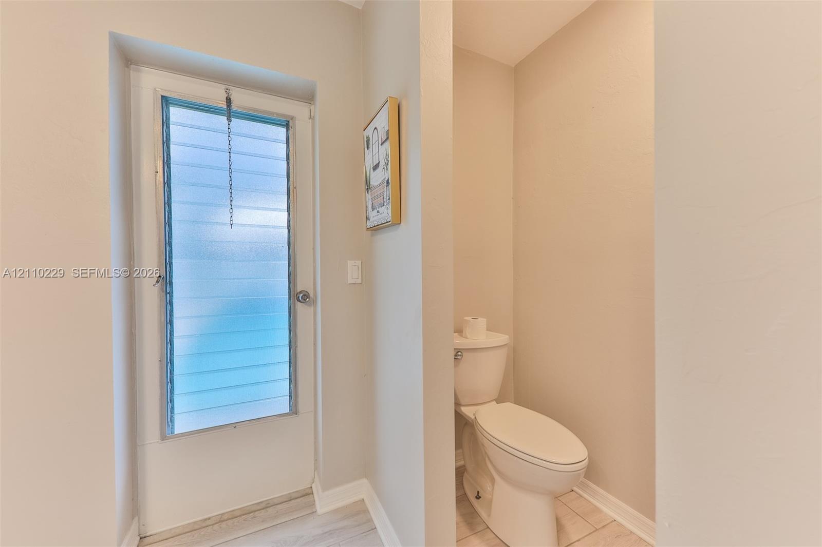 Full-height exterior door with frosted horizontal jalousie glass and an elongated white toilet