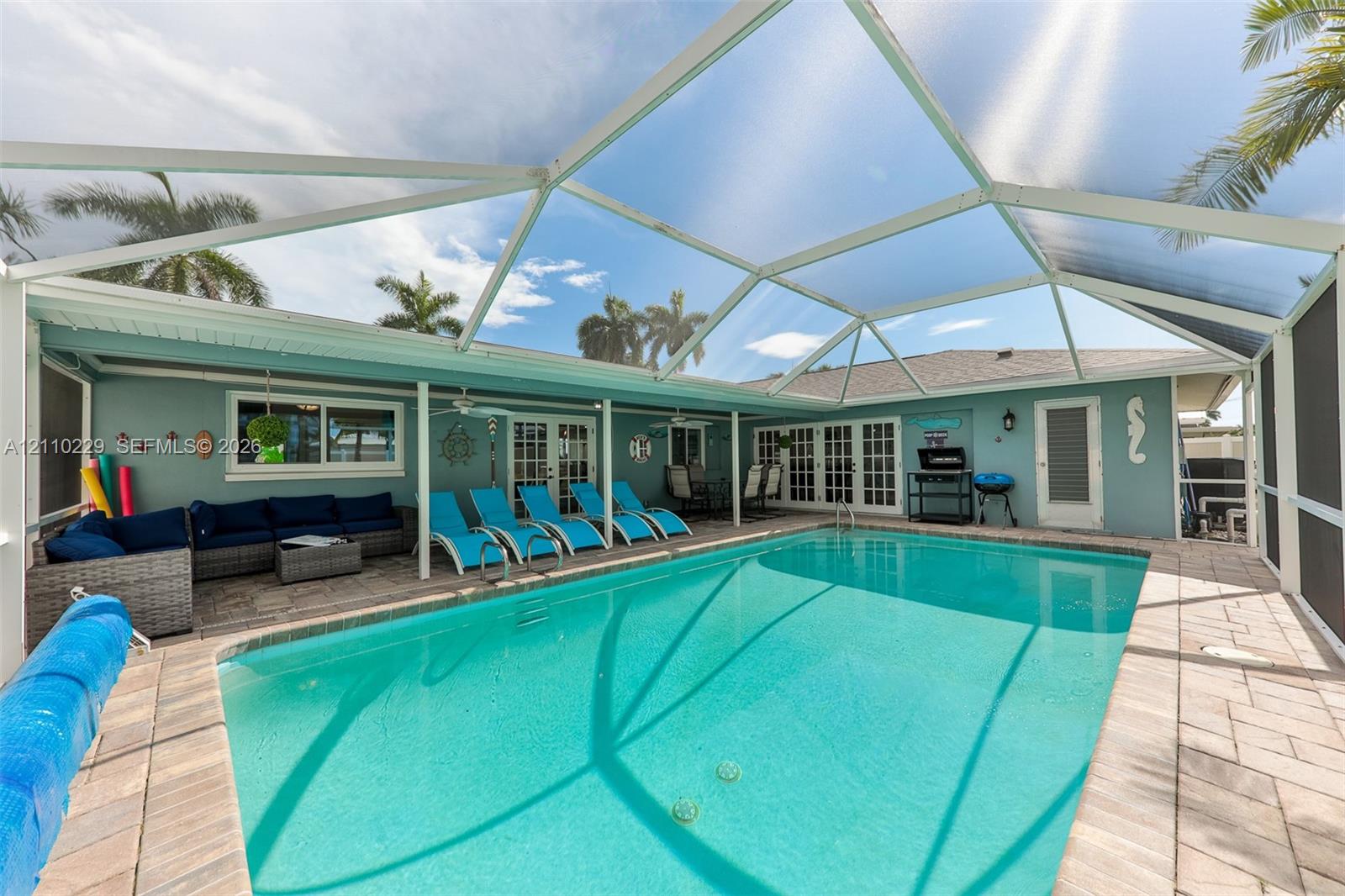 Screened-in pool area featuring a paver deck, white aluminum structural framing, and multiple sets of glass-paned French doors