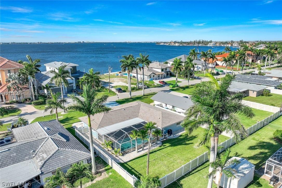 Aerial perspective featuring a waterfront property with an enclosed pool, expansive fenced yard, and mature palm trees