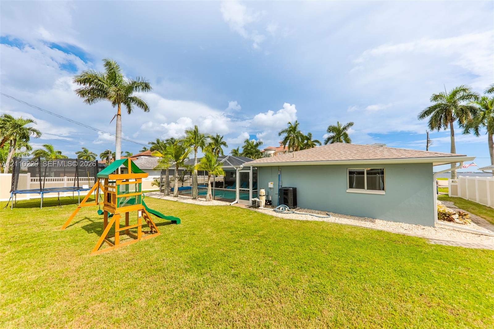 Spacious backyard featuring a manicured lawn, established palm trees, a screened-in swimming pool, and solid vinyl perimeter fencing