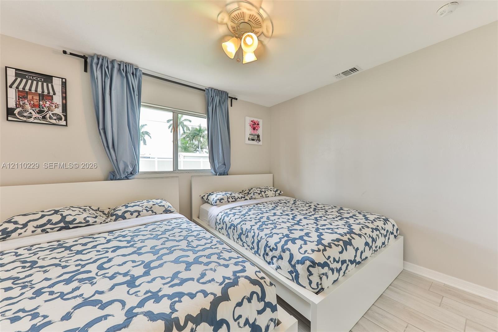 Neutral wall tones, horizontal sliding window with decorative drapery, and wood-finish tile flooring complemented by a multi-light ceiling fixture