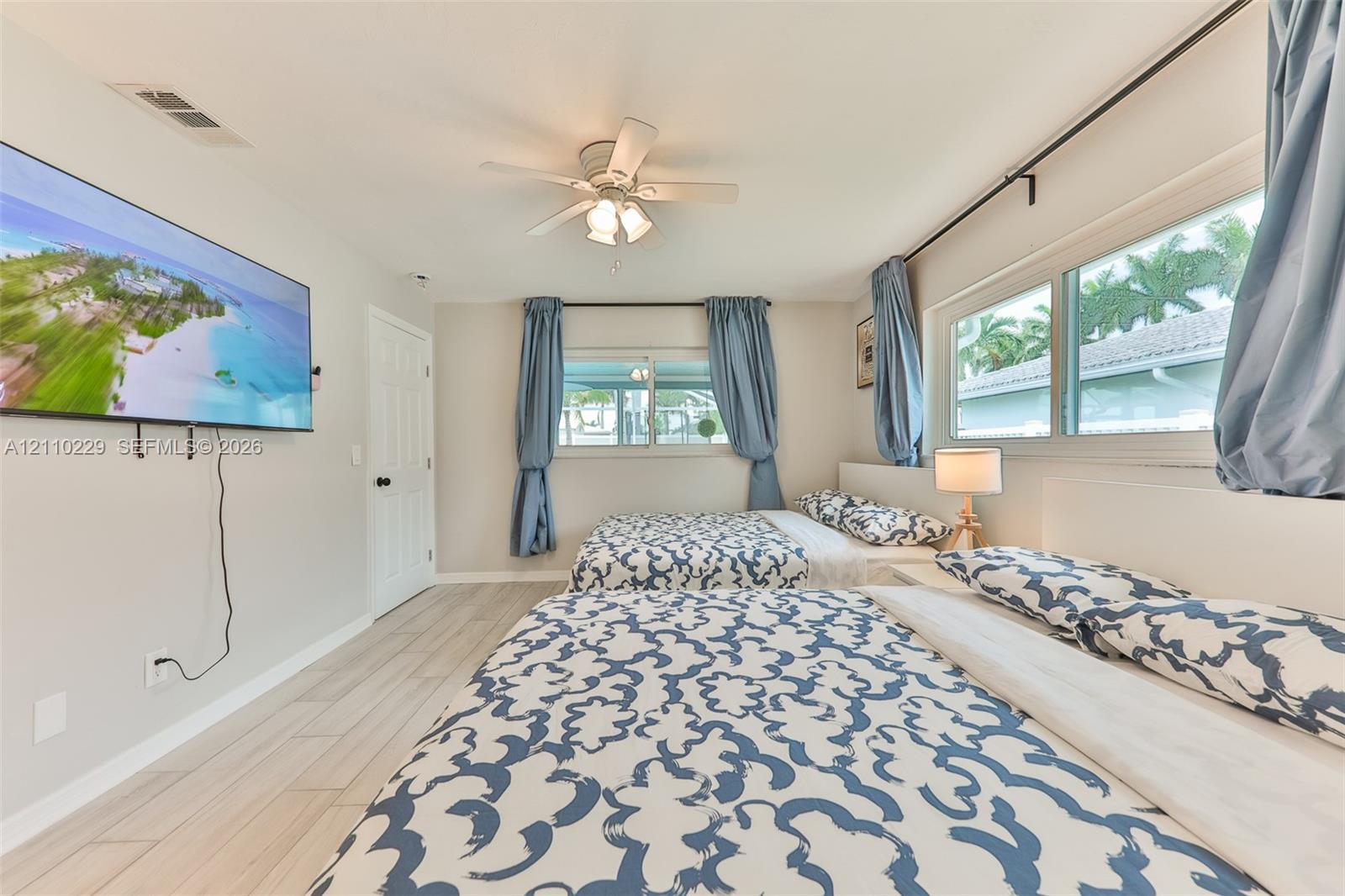 Neutral-toned interior space featuring light-toned wood-finish flooring, a multi-blade ceiling fan with integrated lighting, and multiple horizontal windows