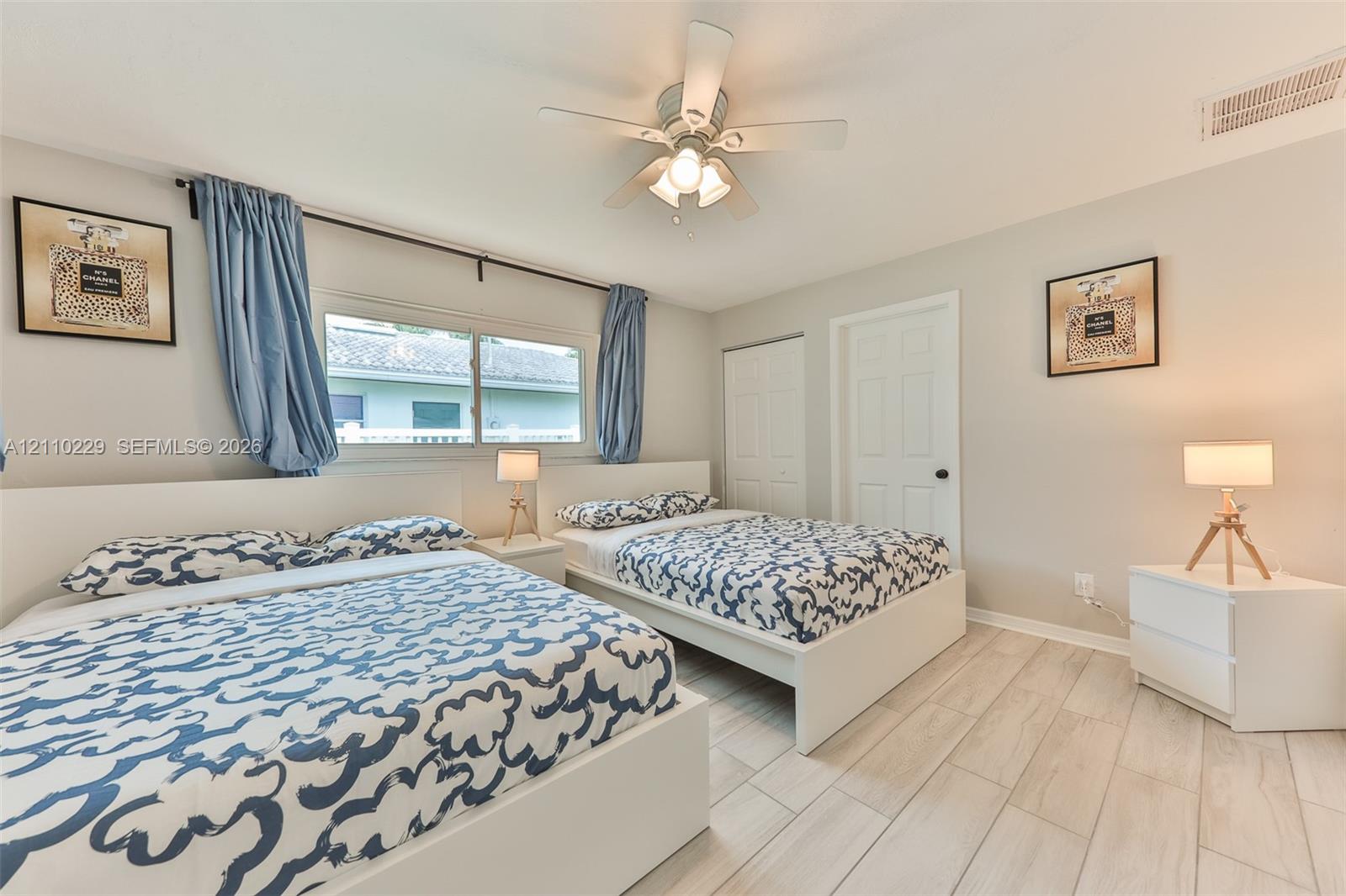 Neutral-toned interior featuring wood-finish tile flooring, a multi-blade ceiling fan, and sliding closet doors with six-panel entry door detail